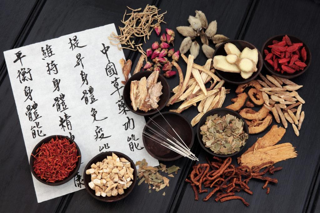 Acupuncture needles with chinese herbal medicine selection and mandarin calligraphy script on rice paper describing the medicinal functions to maintain body and spirit health and balance body energy.